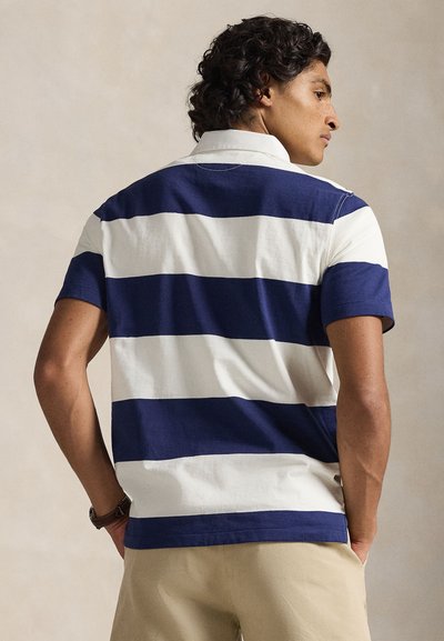 Πόλο μπλούζα με ναυτικό μπλε και λευκές ρίγες, γιακά και κοντά μανίκια, κατασκευασμένη από υφασμάτινο βαμβάκι με υφή και κανονική εφαρμογή.