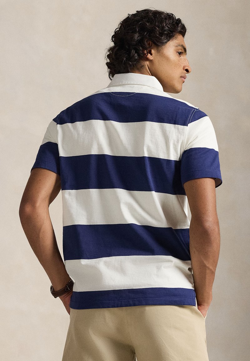 Polo à rayures bleu marine et blanches avec col et manches courtes, affichant un matériau en coton texturé et une coupe régulière.