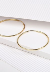 Boucles d'oreilles en or en forme de cercle exposées sur un carton blanc texturé, présentant une forme ronde lisse et une finition fine et polie.