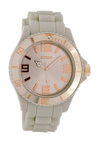 Montre en silicone gris clair avec un cadran rond, des accents en or rose, de grands marqueurs numériques et une lunette texturée. Présente une fenêtre de date à 6 heures.