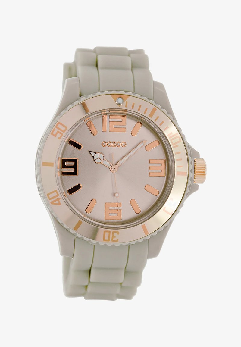 Montre en silicone gris clair avec un cadran rond, des accents en or rose, de grands marqueurs numériques et une lunette texturée. Présente une fenêtre de date à 6 heures.