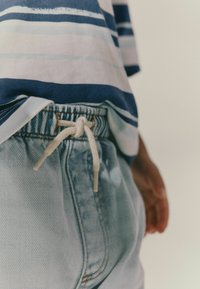 Randig kortärmad skjorta i blått och vitt, i kombination med ljusblå denimshorts, som har en dragsko i midjan med en knuten repdetalj.