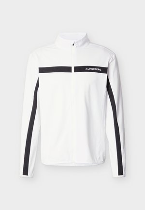 Balta rāvējslēdzēja jaka ar melnu horizontālu joslu krūtīs un vertikālām joslām uz piedurknēm, uz krūtīm ar zīmola "J. Lindeberg" logo.