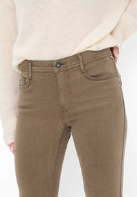 Jeans in denim marrone con un design slim, cinque tasche e chiusura con bottone. Il tessuto ha una texture liscia e dettagli di cucitura discreti.