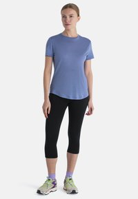 Camiseta de manga corta azul claro con escote redondo, combinada con leggings capri negros y zapatillas deportivas multicolores.