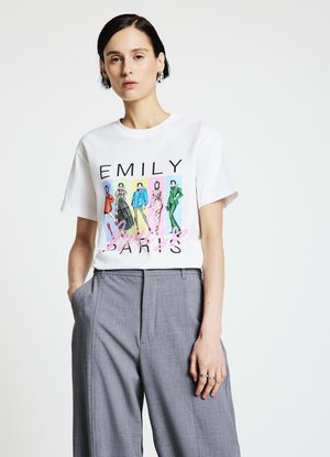 Weißes Baumwoll-T-Shirt mit einer bunten Grafik von Modefiguren und dem Text "EMILY IN PARIS", kombiniert mit grauen Hosen.