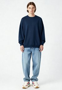 Tamsiai mėlynas per didelis d�žemperis su raštuotais manžetais ir apatine dalimi, derinamas su šviesiai mėlynomis plačiomis džinsomis ir baltomis sportinėmis bateliais su raudonais ir mėlynais akcentais.