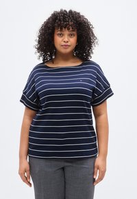 Μπλε μπλούζα με ρίγες και κοντά μανίκια, κατασκευασμένη από μαλακό ύφασμα. Διαθέτει λευκές οριζόντιες γραμμές και στρογγυλεμένο λαιμόκοψη.