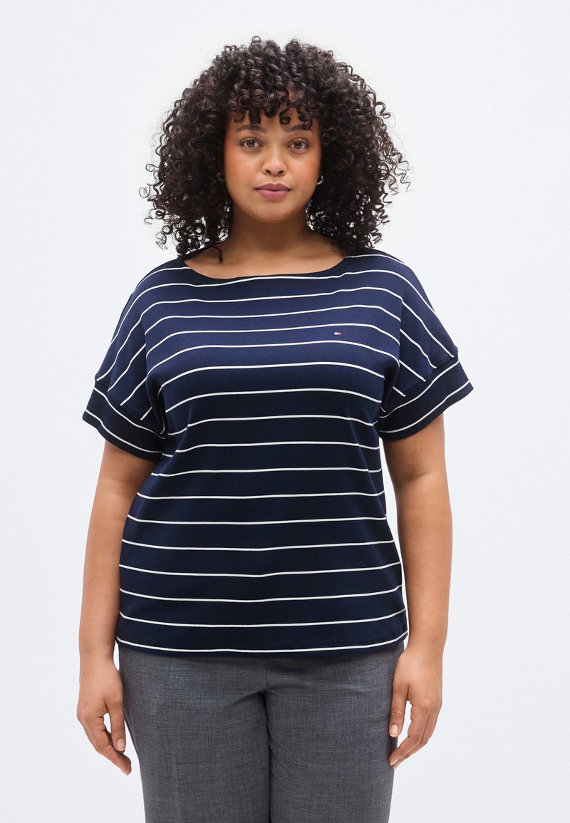 Μπλε μπλούζα με ρίγες και κοντά μανίκια, κατασκευασμένη από μαλακό ύφασμα. Διαθέτει λευκές οριζόντιες γραμμές και στρογγυλεμένο λαιμόκοψη.