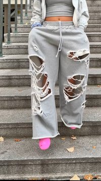 Sivé tepláky s veľkými, nepravidelnými roztrhnutiami a strapcami na okrajoch, s elastickým pásom; nosené s jasne ružovou obuvou na schodoch.