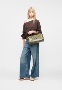Bolso de cuero verde oliva con acento en forma de estrella, combinado con un sudadera marrón de gran tamaño y jeans de mezclilla azul de pierna ancha.