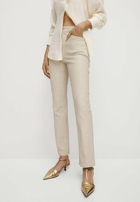 Beżowe dopasowane spodnie o gładkiej fakturze i średnim stanie. Połączone z metaliczno-złotymi szpilkami w szpic.