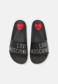 Black slide sandals featuring a textured footbed, embellished with rhinestones spelling "LOVE MOSCHINO" and a red heart logo on the strap.