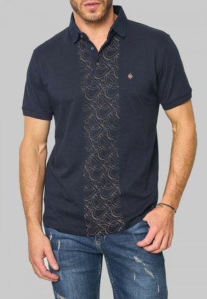 Polo shirt bleu marine avec un panneau central à motif comportant un design répété dans une teinte contrastante. Manches courtes et col classique.