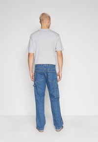 Tricou gri cu mânecă scurtă, asortat cu blugi cargo largi, de culoare albastră, având multiple buzunare și o croială lejeră. Material neted, siluetă casual.