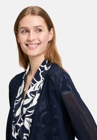 Marineblaues Netz-Cardigan mit einem fließenden, weiß und marineblau gemusterten Schal. Besitzt einen lockeren Schnitt und ein offenes Design, das die leichte Stofftextur zur Geltung bringt.