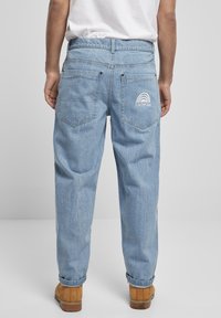 Světle modré džínové kalhoty s uvolněným střihem, s vysokým pasem a dvěma zadními kapsami. Na zadní kapse je bílá výšivka duhy "SOUTHPOL".