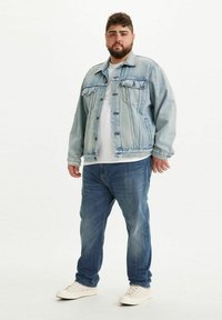 Vaaleansininen farkkutakki, jossa on kaksi rintataskua, päällä valkoinen paita, yhdistettynä sinisiin farkkuihin ja vaaleisiin tennareihin. Yksinkertainen valkoinen tausta.