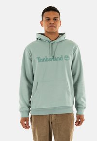 Felpa con cappuccio verde menta, dotata di tasca frontale, con logo "Timberland" ricamato e emblema dell'albero. Tessuto morbido con polsini a coste.