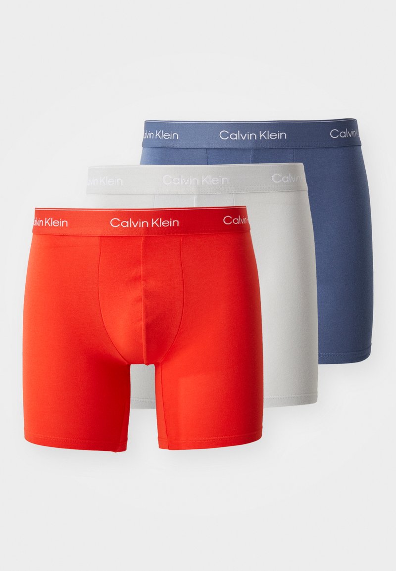 Trois paires de boxers pour hommes : rouge, gris clair et bleu marine. Fabriqués en tissu doux avec des ceintures élastiques arborant le logo Calvin Klein.