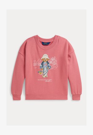 Rosa Sweatshirt mit einer Grafik eines Bären, der einen Hut, ein gestreiftes Hemd, eine Jeansjacke trägt und einen Korb hält, mit Hausumriss im Hintergrund.