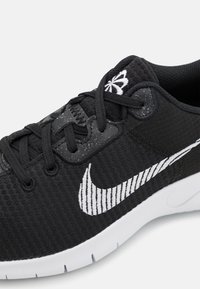 Scarpa sportiva nera con upper testurizzato, caratterizzata da un distintivo swoosh bianco di Nike e lacci sottili. La suola è bianca con un motivo di battistrada visibile.