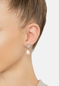 Boucles d'oreilles en argent sterling avec un design de papillon, ornées de petites pierres précieuses transparentes et d'un pendentif nacré suspendu.