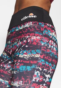 Ellesse legging met een hoge zwarte tailleband bevat kleurrijke abstracte patronen in rood, blauw en wit tegen een zwarte achtergrond.