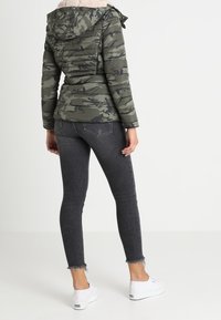 Grøn camouflage pufferjakke med hætte, suppleret med en lys kunstpels krave; parret med sorte skinny jeans og hvide sneakers.