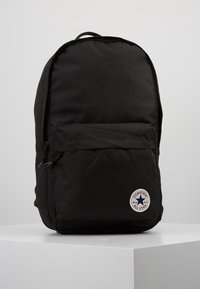Sac à dos noir en tissu lisse et durable. Dispose d'une poche avant et d'un patch logo en forme de cercle avec une étoile. Forme simple et arrondie.
