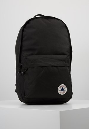 Sac à dos noir en tissu lisse et durable. Dispose d'une poche avant et d'un patch logo en forme de cercle avec une étoile. Forme simple et arrondie.