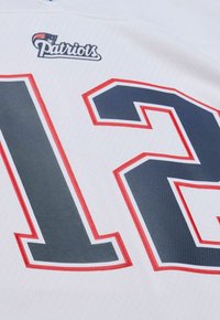 Weißes Sporttrikot mit einer marineblauen "12", umrandet in rot. Oben mit dem Logo der "Patriots". Hergestellt aus strukturiertem Stoff, geeignet für Sportbekleidung.