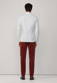 Camicia a maniche lunghe a quadri in bianco e blu, con una vestibilità slim e polsini a bottoni, abbinata a pantaloni in velluto a coste rossi e scarpe scure.