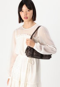 Dark brown leather handbag with gathered design and two front pockets. Short strap, smooth texture, and subtle sheen.