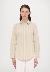 Beige stripete skjorte med lange ermer, rundet kant og myk tekstur. Har hvite vertikale striper og klassisk krage.