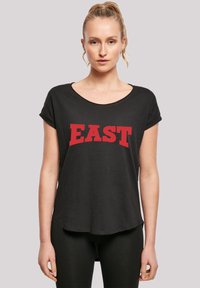 Svart T-skjorte med kort erm, rund hals og buet rød "EAST" tekst. Myk stoff med avslappet passform og litt lengre bakstuss.