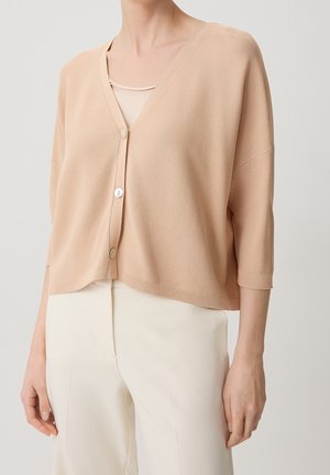 Cardigan court rose clair avec col en V, manches trois-quarts et deux boutons à l'avant. Texture douce, coupe décontractée, associé à un pantalon couleur crème.