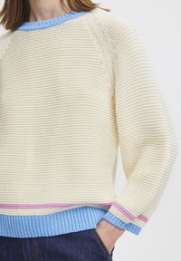 Cremfarbener Strickpullover mit blauen und rosa Rippakzenten am Kragen und Saum. Besitzt einen entspannten Schnitt und ein texturiertes Muster im gesamten Design.