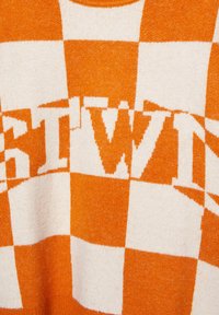 Sveter s kostkovaným vzorom v oranžovej a krémovej farbe, ktorý obsahuje výrazné slovo v kontrastnom dizajne, s jemnou textúrou a okrúhlym výstrihom.