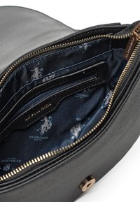Interno di una borsa a tracolla in pelle sintetica nera con fodera blu navy, caratterizzato da un motivo ripetuto del logo della U.S. Polo Assn. e tasche con zip. Cerniera in tonalità oro.