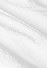 Tissu blanc avec une subtile broderie florale en relief et des plis doux, créant une apparence texturée et délicate.