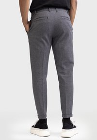 Pantalon texturé gris avec une coupe fuselée, présentant des poches arrière et des poignets retroussés, associé à des baskets noires.