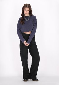 Przycięta granatowa bluzka z długim rękawem z miękkiego materiału, zestawiona z luźnymi czarnymi spodniami. Dodatki obejmują warstwowe srebrne łańcuszki oraz masywne czarne obuwie.