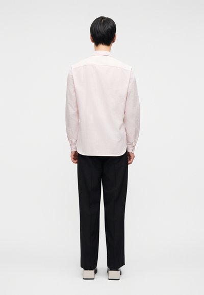 Ροζ ανοιχτόχρωμο ριγέ πουκάμισο με μακριά μανίκι α, πίσω πατ και κυρτό τελείωμα, με μανσέτες με κουμπιά, συνδυασμένο με μαύρο παντελόνι και ανοιχτόχρωμα παπούτσια.