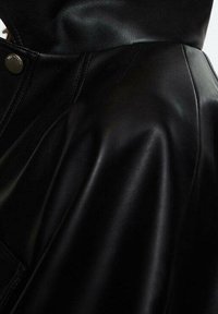 Czarna skórzana kurtka o gładkiej teksturze, dopasowanym kroju i widocznym szwie wzdłuż szwu na ramieniu i kołnierza.