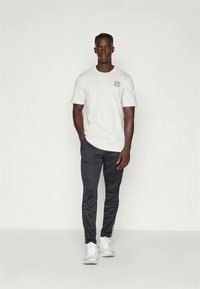 T-shirt branca de algodão e calças de treino cinza-escuras, com riscas laterais, contrastadas com sapatilhas brancas. Design simples e corte descontraído.