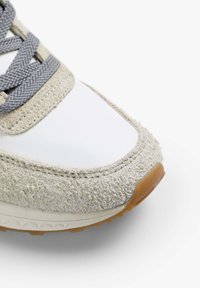 Zapatillas con un upper sintético blanco y suave, cordones gris, y acentos de gamuza gris clara; puntera redonda con suela texturizada y suela de goma natural.