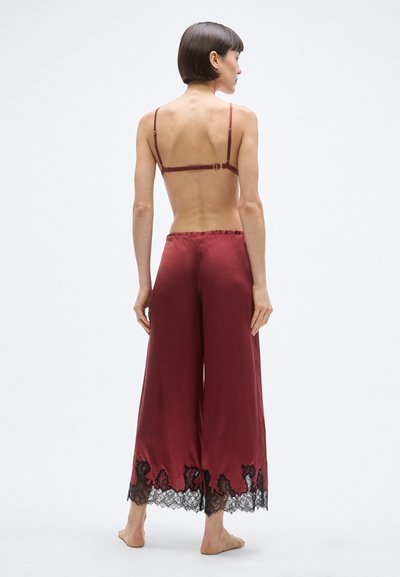 Bordowy satynowy zestaw piżamowy z krótkim topem na cienkich ramiączkach i szerokimi spodniami, ozdobiony czarną koronką przy krawędzi.