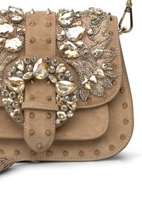 Sac à main en suédine beige présentant un design orné de bijoux avec plusieurs strass et des clous décoratifs. Comprend une fermeture à boucle décorative.
