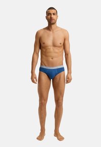 Heren stringondergoed in het blauw, gemaakt van zacht materiaal met een grijze elastische tailleband met logo-tekst. Aangepast ontwerp en gestroomlijnde vorm.